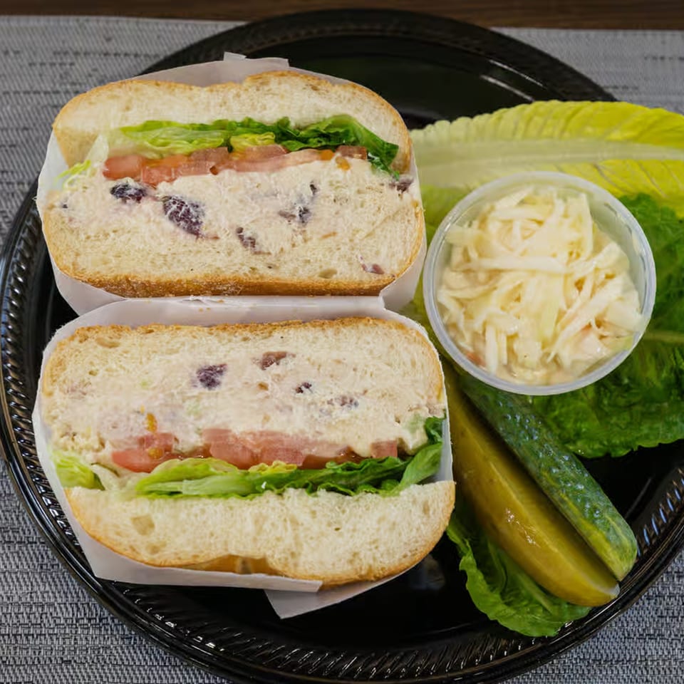 Two Bagel Boys chicken salad sandwiches with lettuce, tomato, coleslaw, and pickles on a black tray.