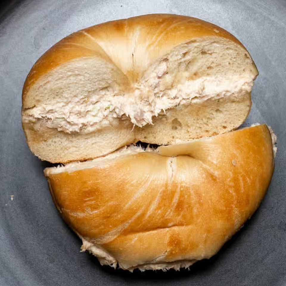 A Bagel Boys bagel, sliced in half and filled with cream cheese, on a dark surface.