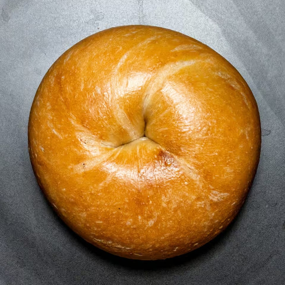 A single golden-brown Bagel Boys bagel with a shiny crust, centered on a dark background.