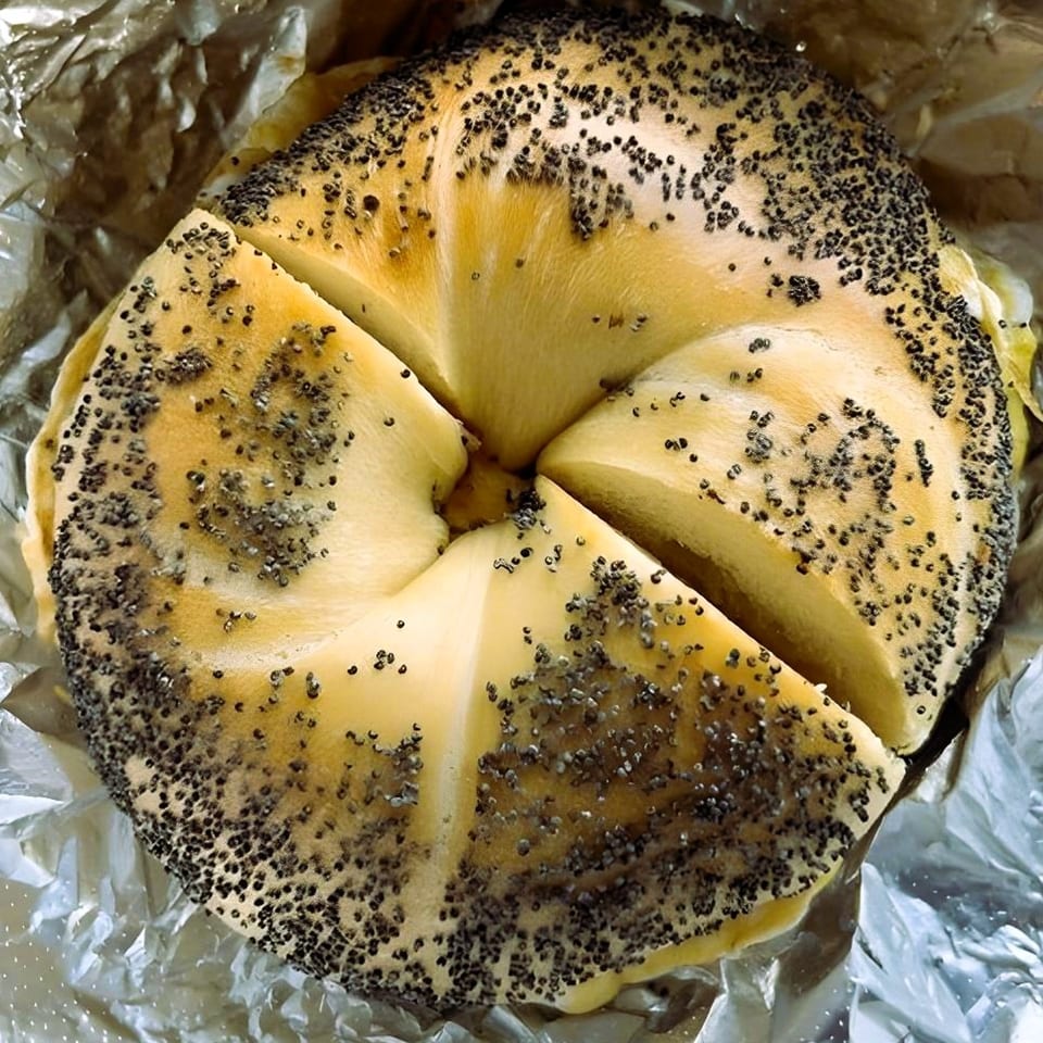 Bagel Boys' poppy seed bagel, sliced into quarters, resting on crinkled aluminum foil.
